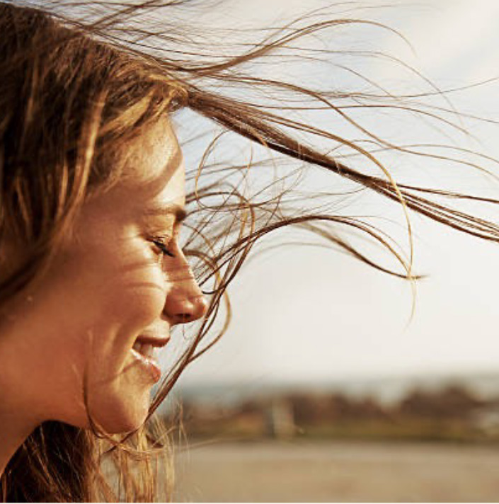 Photo d'une femme dans la nature fermant les yeux, épanouie et détendue, symbole du wellaging et de l'acceptation de soi, inspiration Philosophale